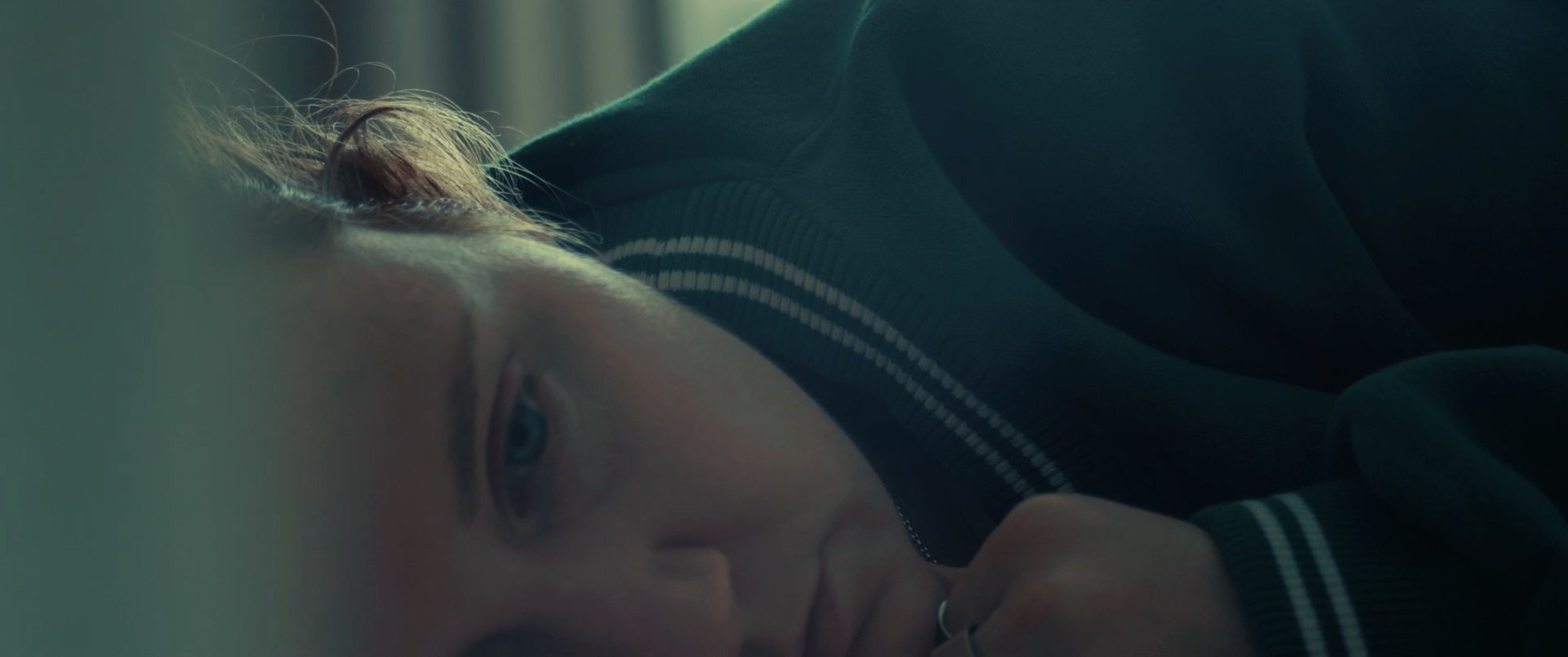 Film still: a woman lying on her side, face in close-up, lit in cool green tones