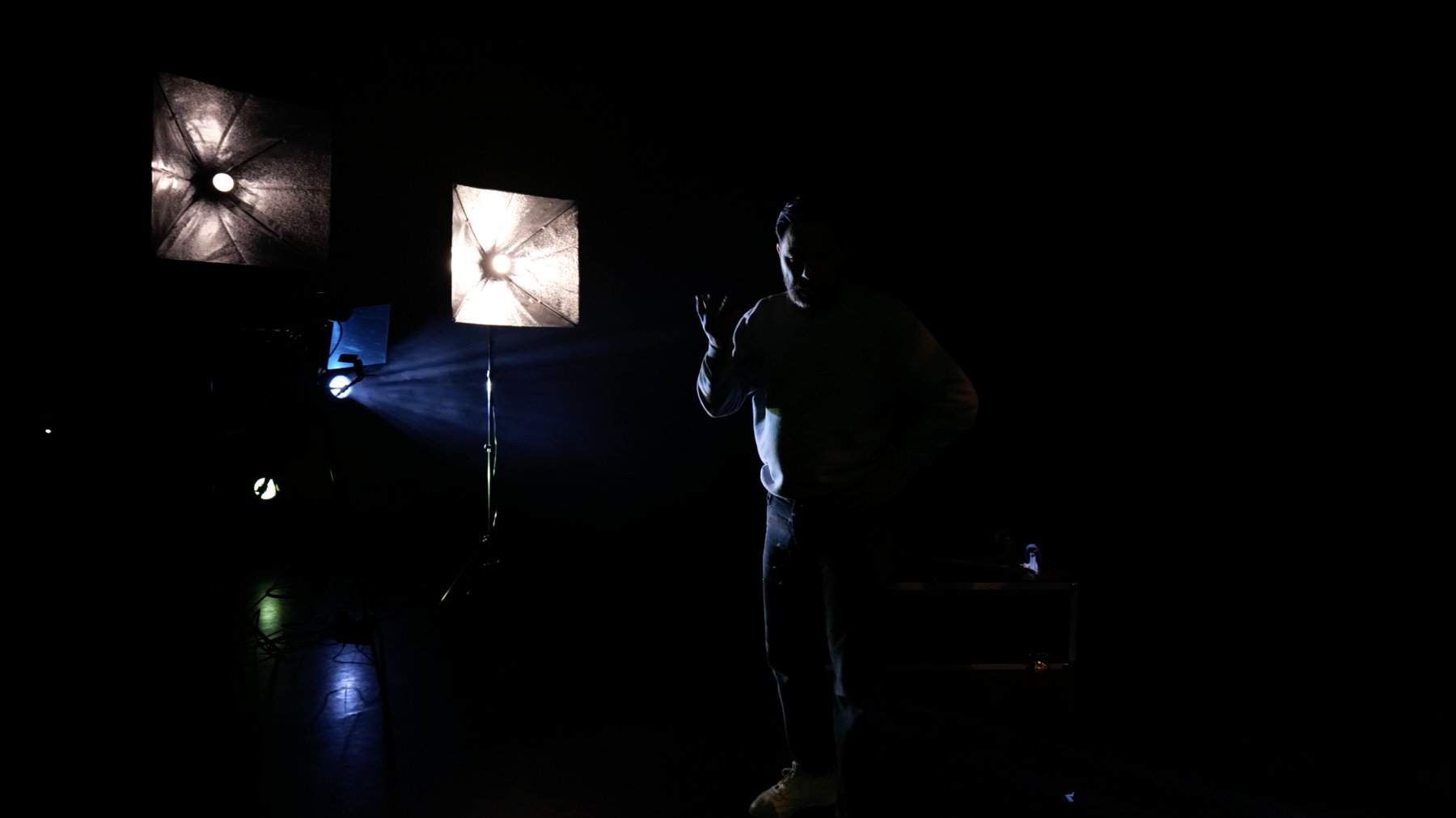 Dark stage with two lit softboxes, a blue beam of light and a performer in silhouette