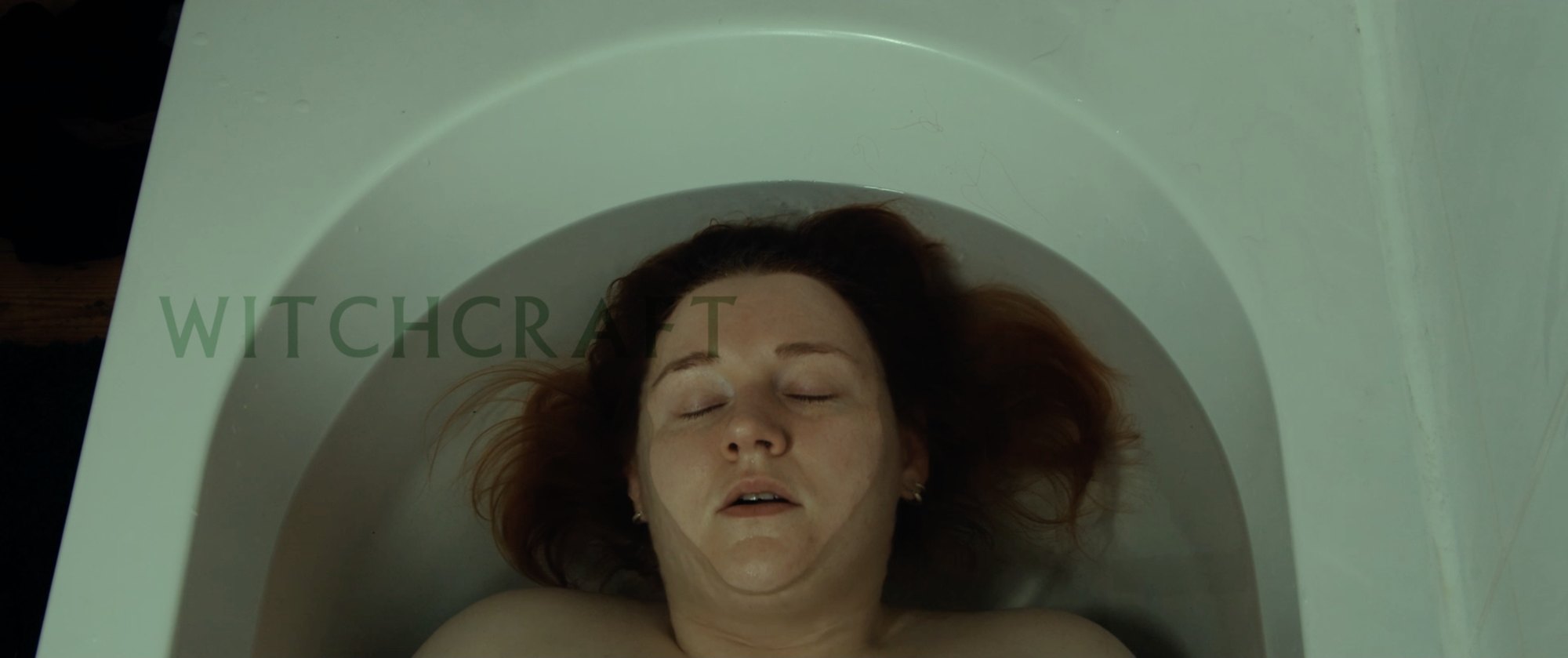 Film still: a woman lying in a bathtub, seen from above