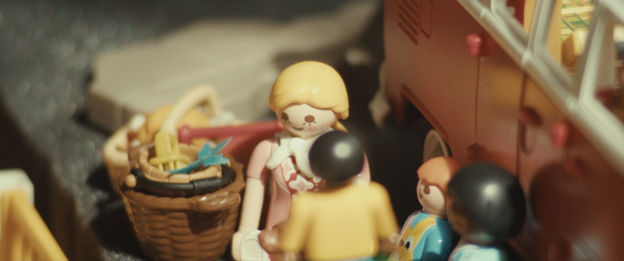 Film still from They’re Taking The Tiles Off The Building: toy figures of a woman and children beside a toy camper van, in warm light