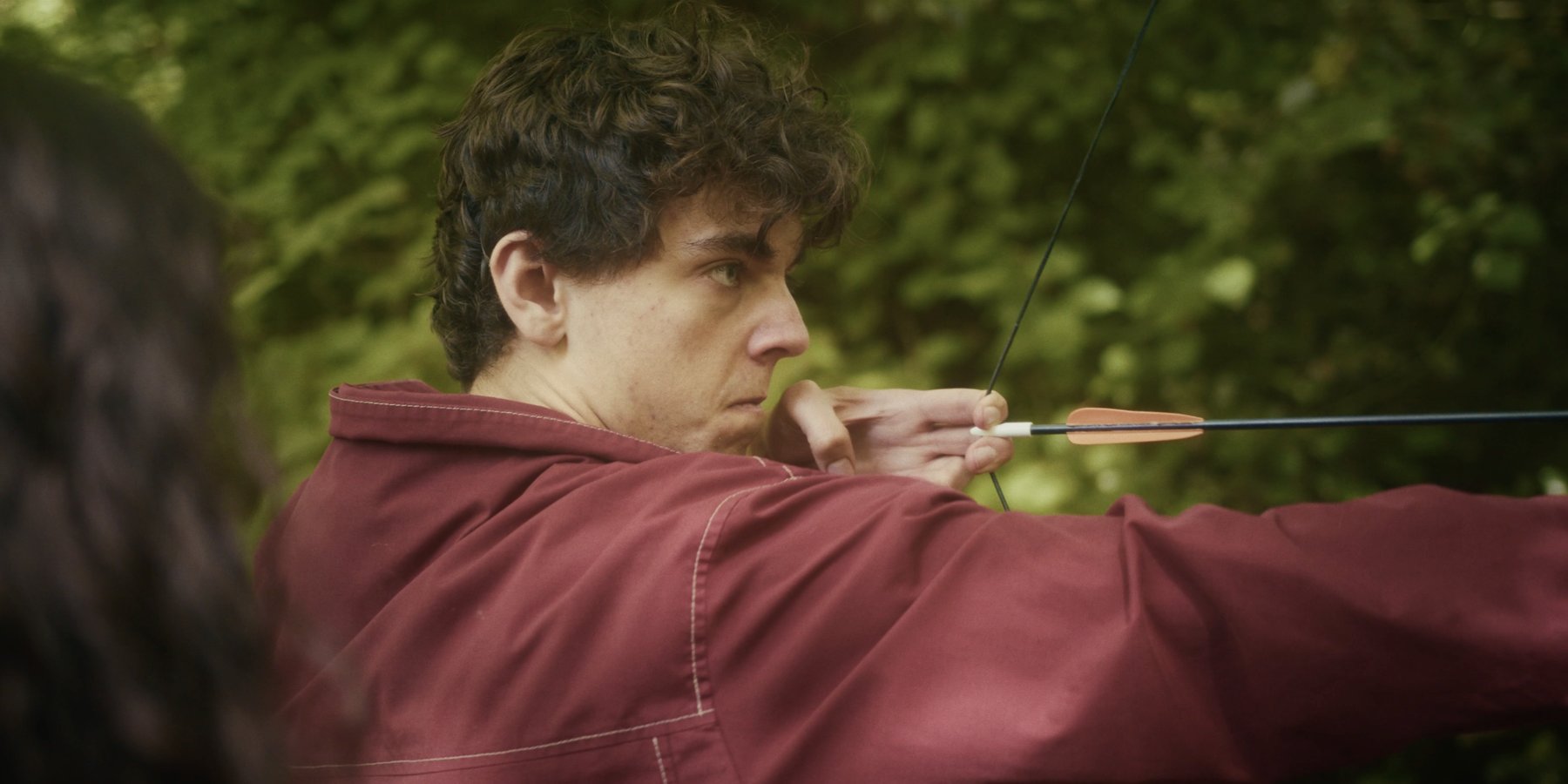 Close profile of a young man concentrating as he draws an arrow back on a bow, in woodland